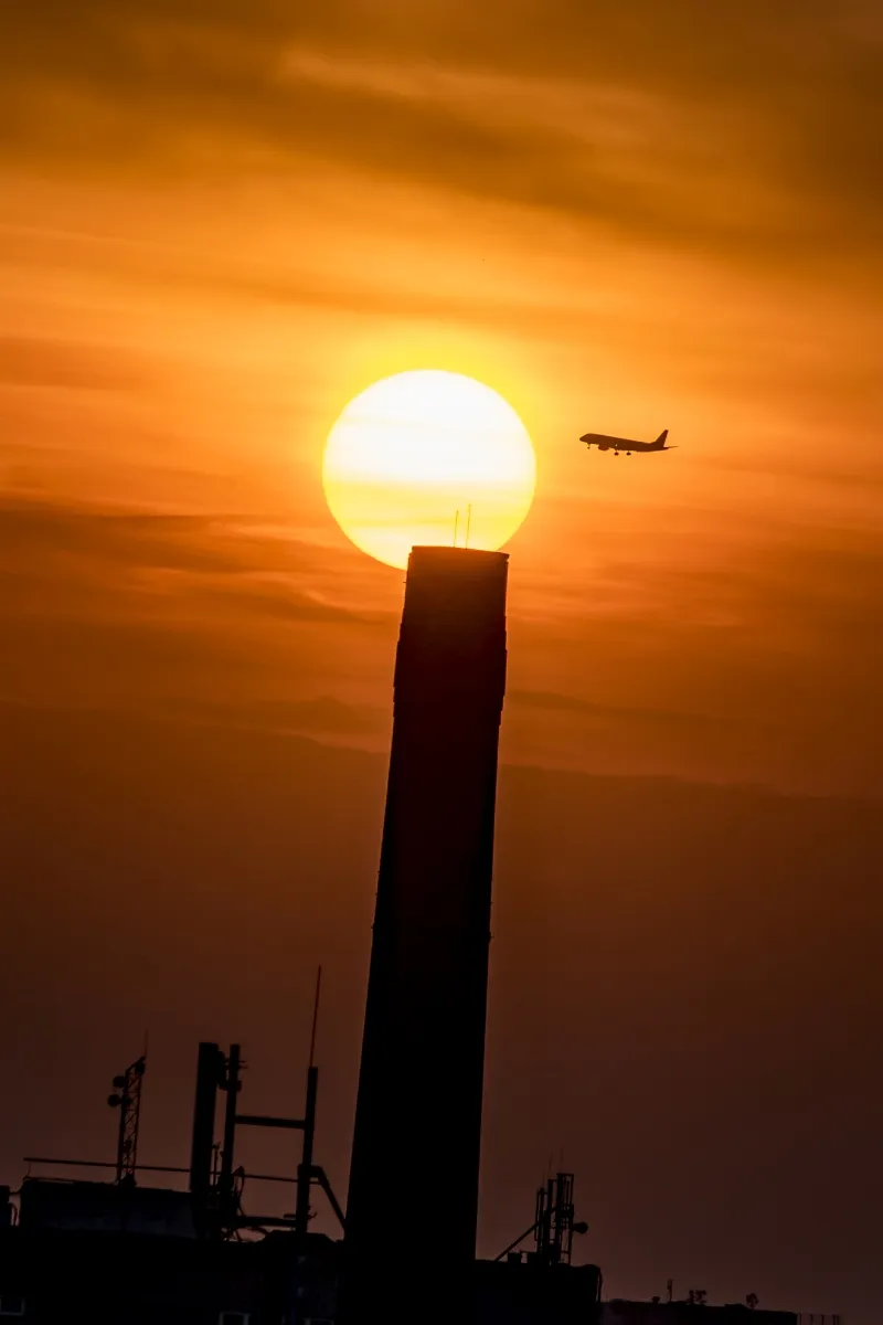 Airplane passing a setting sun aligned above a dark chimney